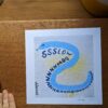 an art print of a blue snake is on a desk next to a hand and a plant pot